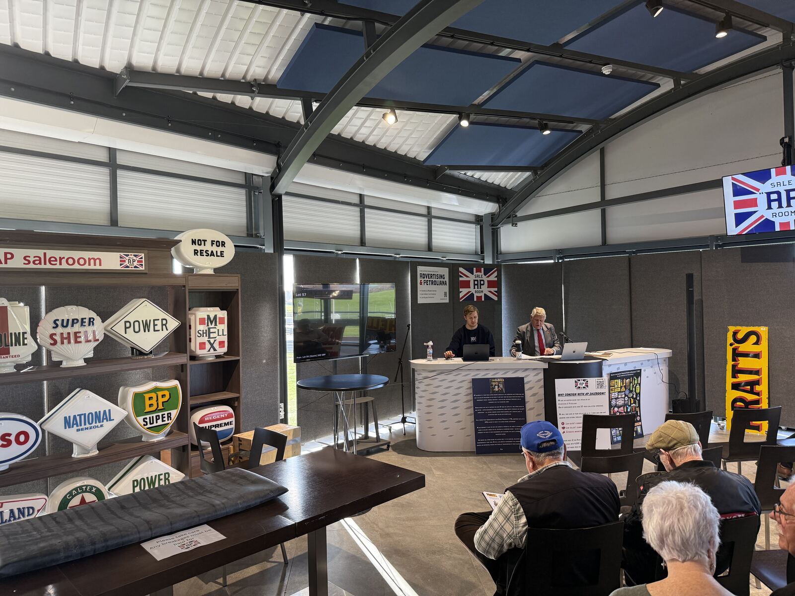 A live AP Saleroom auction under way in the BARC Clubhouse, with the rostrum and shelves of petrol pump globes