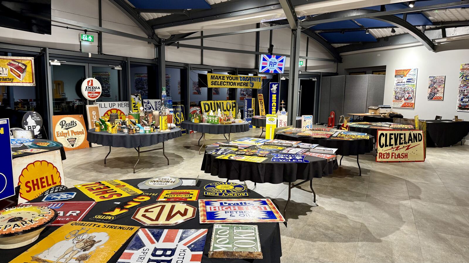 Tables of vintage enamel advertising signs laid out for viewing inside the BARC Clubhouse